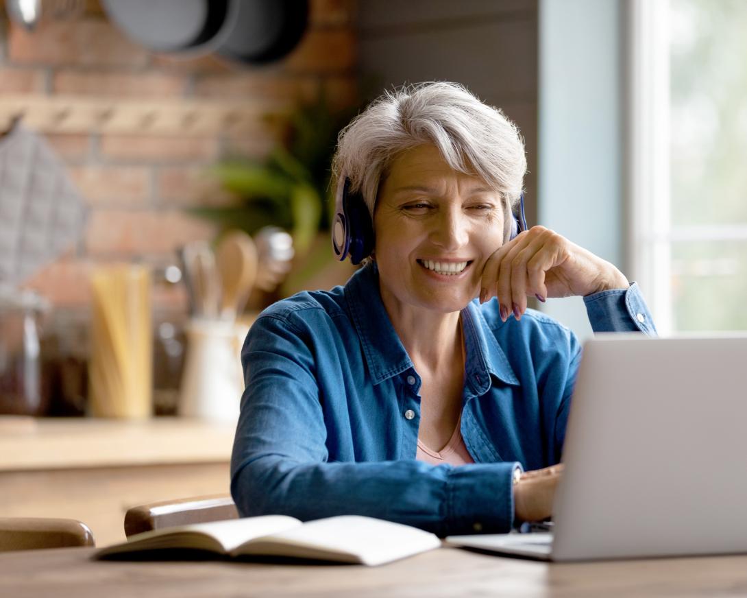 glimlachende vrouw telefoneert met headset en laptop in de keuken