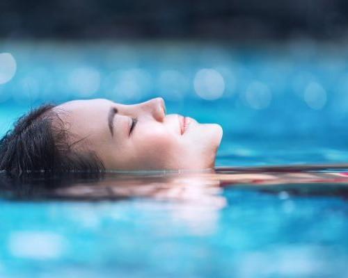 vrouw drijft op de rug met ogen toe in stil water 