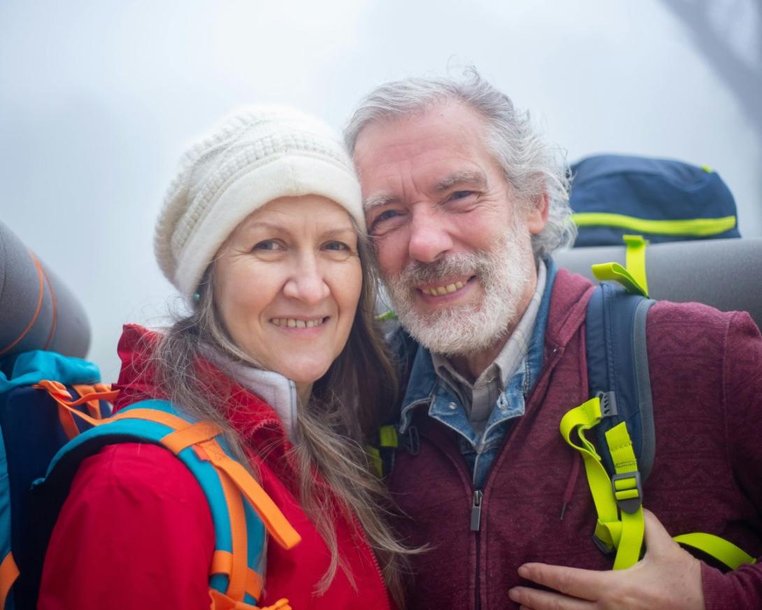Oudere man en vrouw met rugzak poseren innig en blij voor de foto